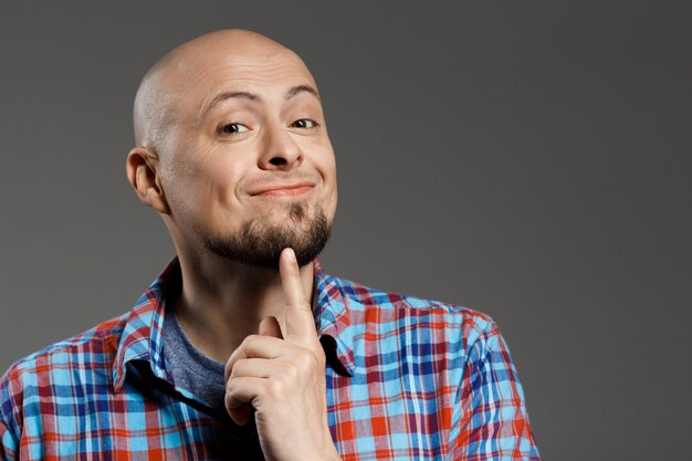 Retrato de hombre guapo pensativo alegre en camisa a cuadros sonriendo a la cámara sobre la pared gris