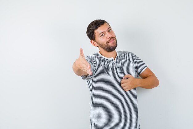 Retrato de hombre guapo que ofrece apretón de manos para saludar en camiseta y mirar vista frontal amigable