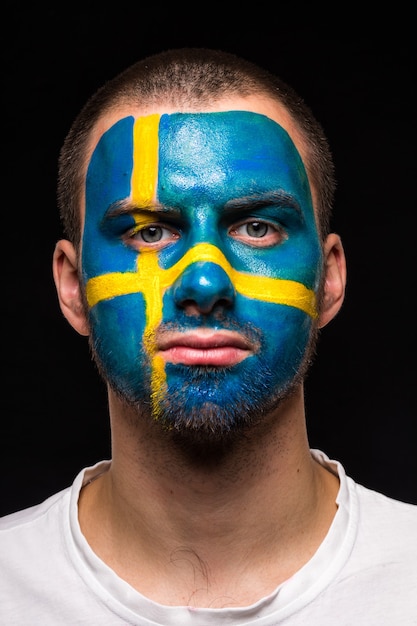 Foto gratuita retrato de hombre guapo rostro partidario fan del equipo nacional de suecia con cara de bandera pintada aislado sobre fondo negro. fans de las emociones.