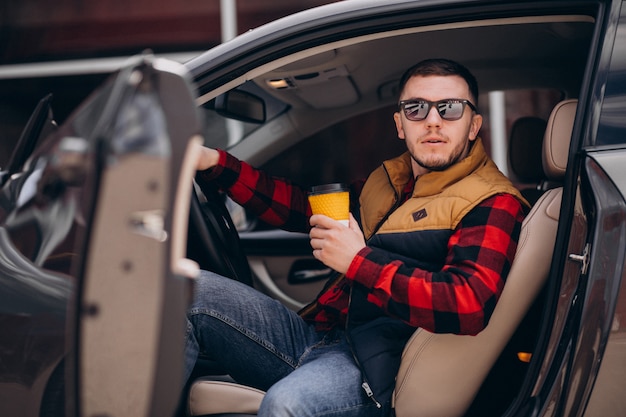 Retrato de hombre guapo sentado en el coche y tomando café