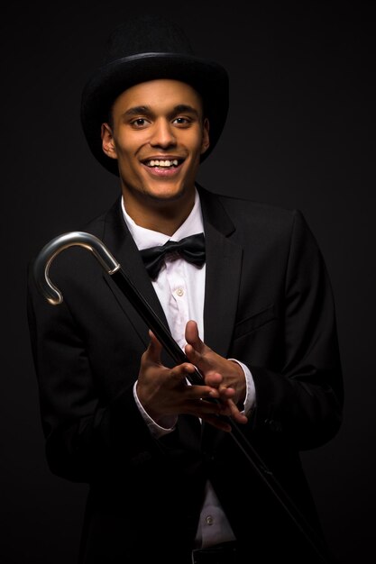 Retrato de hombre guapo con sombrero de copa sonriendo para la cámara y sosteniendo el bastón