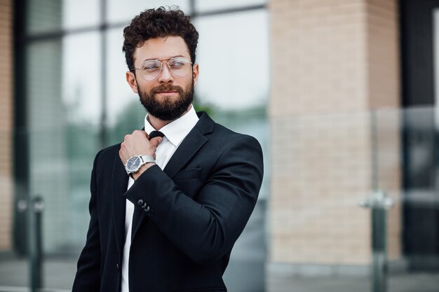 Retrato de un hombre guapo con un traje negro con un reloj en la mano