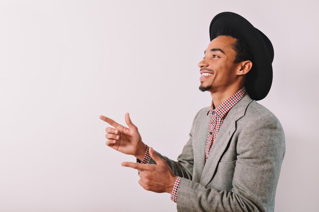 Retrato de hombre guapo viste camisa a cuadros sombrero negro y chaqueta gris de pie sobre gris