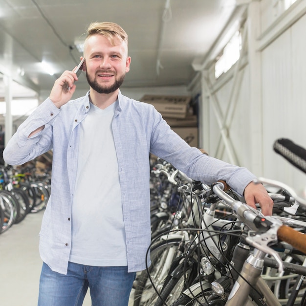 Retrato de un hombre hablando por teléfono inteligente en el taller de bicicletas