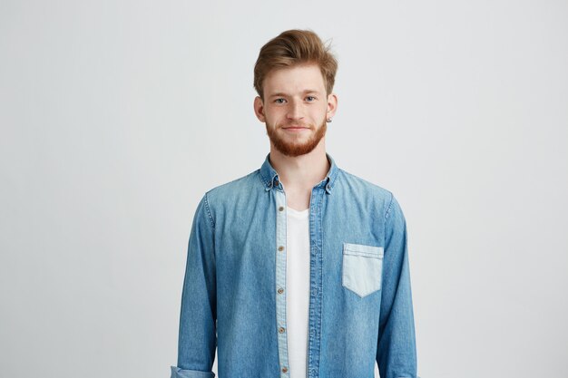 Retrato del hombre hermoso joven en camisa de la mezclilla que sonríe mirando la cámara.