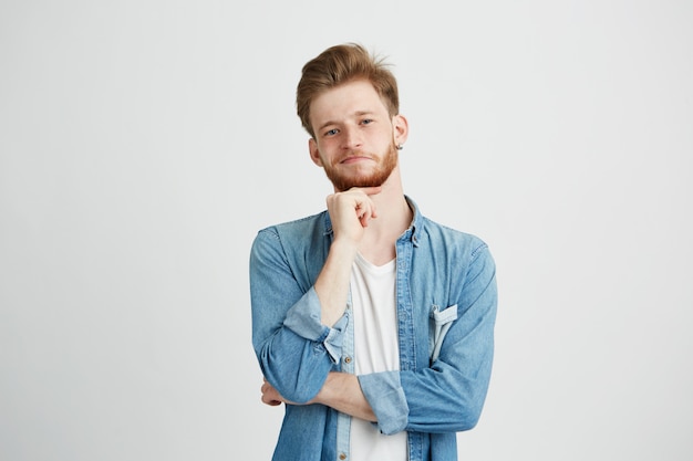 Retrato del hombre hermoso joven confiado con la barba que piensa con la mano en la barbilla.