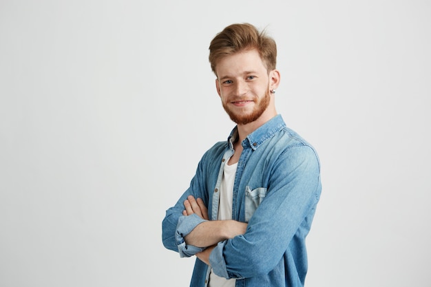 Retrato del hombre hermoso joven confidente que sonríe con los brazos cruzados.