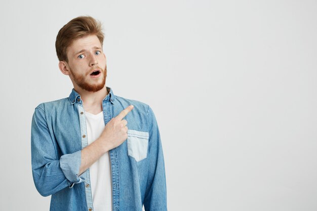 Retrato del hombre hermoso joven sorprendido con la boca abierta que señala el dedo para arriba.