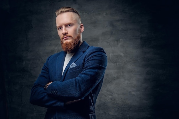 Retrato de hombre hipster pelirrojo barbudo vestido con una chaqueta azul sobre fondo gris.