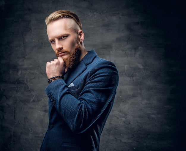 Retrato de hombre hipster pelirrojo barbudo vestido con una chaqueta azul sobre fondo gris.