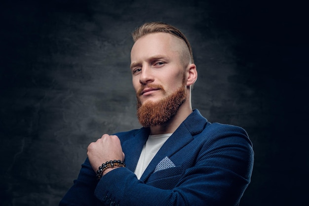 Retrato de hombre hipster pelirrojo barbudo vestido con una chaqueta azul sobre fondo gris.