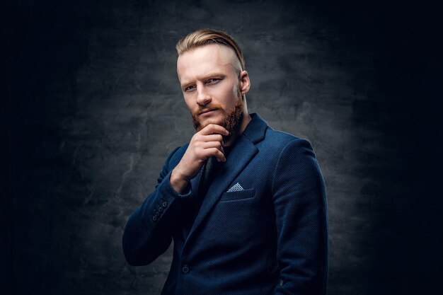 Retrato de hombre hipster pelirrojo barbudo vestido con una chaqueta azul sobre fondo gris.