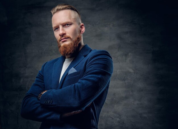 Retrato de hombre hipster pelirrojo barbudo vestido con una chaqueta azul sobre fondo gris.