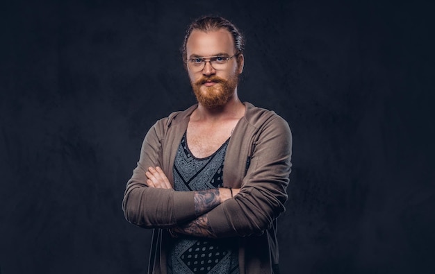 Retrato de un hombre hipster pelirrojo vestido con ropa informal con gafas y barba completa, de pie con los brazos cruzados en un estudio. Aislado en un fondo oscuro.