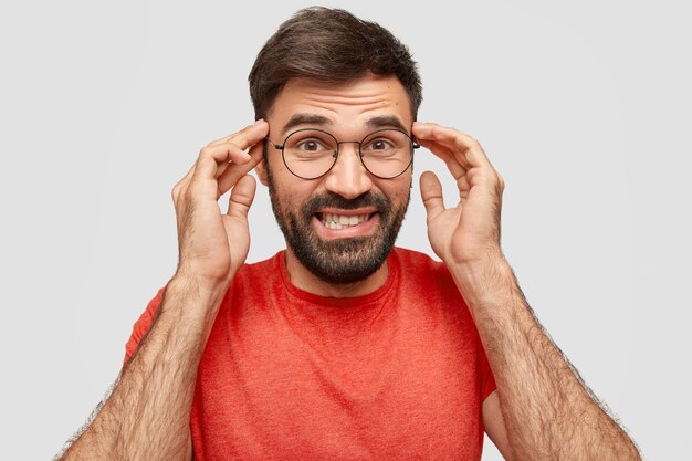 Retrato de hombre inteligente alegre muestra los dientes, mantiene las manos en las sienes, piensa en algo