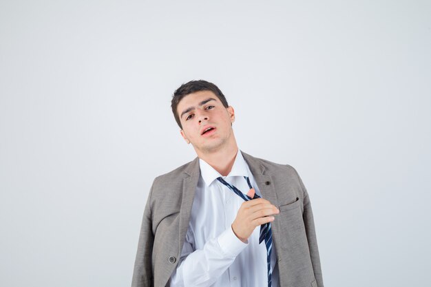 Retrato de hombre joven afloja su corbata mientras posa en camisa, chaqueta, corbata a rayas y mirando fatigada