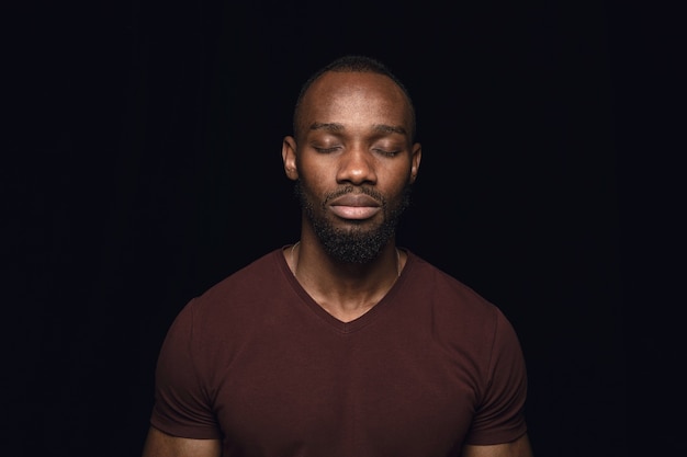 Retrato de hombre joven aislado sobre fondo negro de estudio de cerca. Photoshot de emociones reales del modelo masculino con los ojos cerrados. Considerado. Concepto de expresión facial, naturaleza humana y emociones.