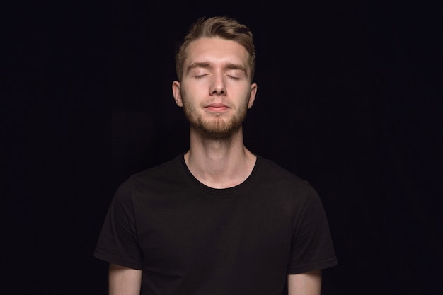 Retrato de hombre joven aislado sobre fondo negro de estudio de cerca. Photoshot de emociones reales del modelo masculino con los ojos cerrados. Considerado. Concepto de expresión facial, naturaleza humana y emociones.