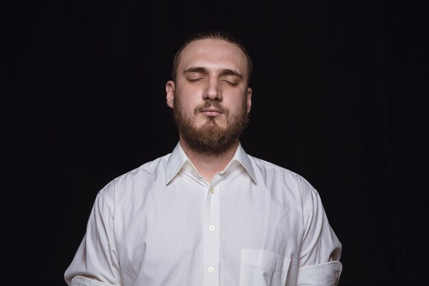 Retrato de hombre joven aislado sobre fondo negro de estudio de cerca. Photoshot de emociones reales del modelo masculino con los ojos cerrados. Considerado. Concepto de expresión facial, naturaleza humana y emociones.