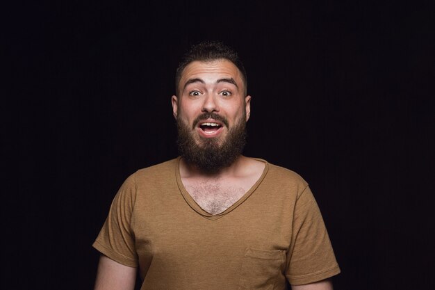 Retrato de hombre joven aislado sobre fondo negro de estudio de cerca. Photoshot de emociones reales del modelo masculino. Preguntándose, emocionado y asombrado. Expresión facial, concepto de emociones humanas.