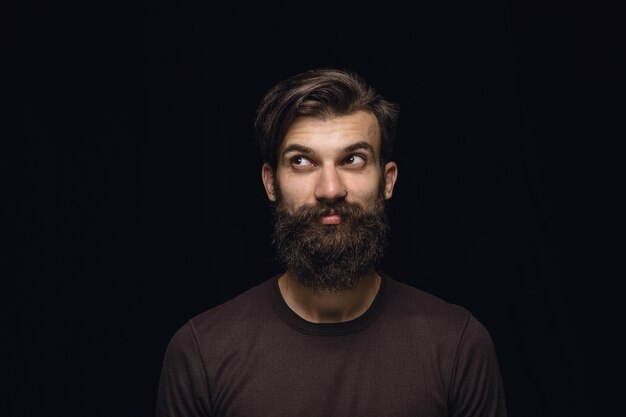 Retrato de hombre joven aislado sobre fondo negro de estudio de cerca. Photoshot de emociones reales del modelo masculino. Soñando y sonriendo, esperanzado y feliz. Expresión facial, concepto de emociones humanas.