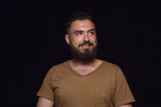 Retrato de hombre joven aislado sobre fondo negro de estudio de cerca. Photoshot de emociones reales del modelo masculino. Soñando y sonriendo, esperanzado y feliz. Expresión facial, concepto de emociones humanas.