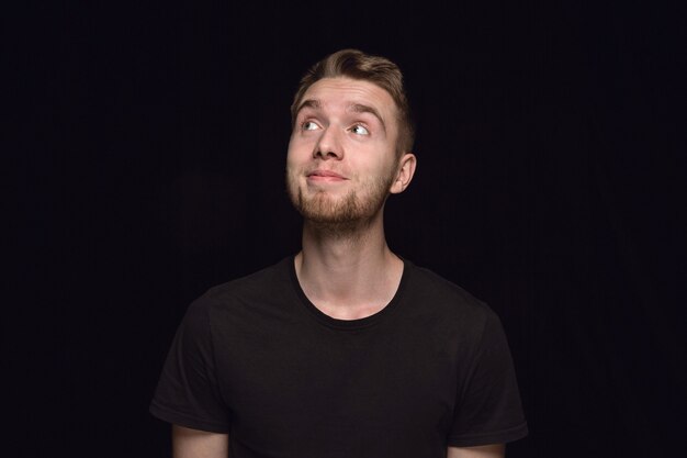 Retrato de hombre joven aislado sobre fondo negro de estudio de cerca. Photoshot de emociones reales del modelo masculino. Soñando y sonriendo, esperanzado y feliz. Expresión facial, concepto de emociones humanas.