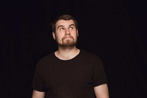 Retrato de hombre joven aislado sobre fondo negro de estudio de cerca. Photoshot de emociones reales del modelo masculino. Soñando y sonriendo, esperanzado y feliz. Expresión facial, concepto de emociones humanas.