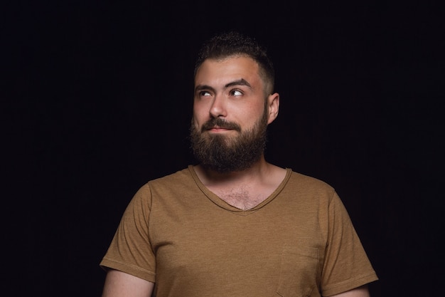 Retrato de hombre joven aislado sobre fondo negro de estudio de cerca. Photoshot de emociones reales del modelo masculino. Soñando y sonriendo, esperanzado y feliz. Expresión facial, concepto de emociones humanas.