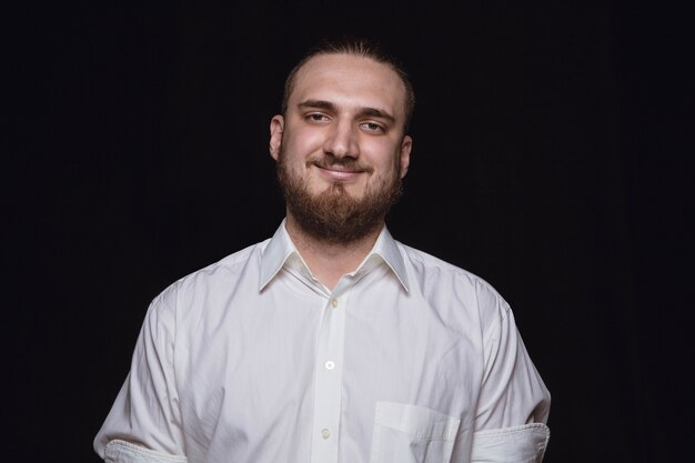 Retrato de hombre joven aislado sobre fondo negro de estudio de cerca. Photoshot de emociones reales del modelo masculino. Sonriendo, sintiéndome feliz. Expresión facial, concepto de emociones humanas puras y claras.