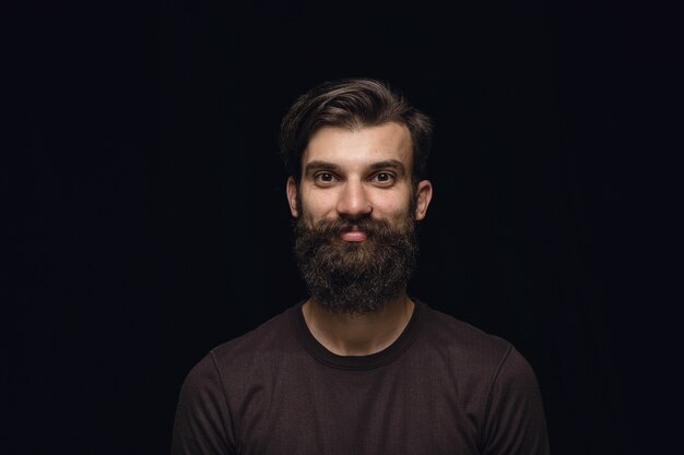 Retrato de hombre joven aislado sobre fondo negro de estudio de cerca. Photoshot de emociones reales del modelo masculino. Sonriendo, sintiéndome feliz. Expresión facial, concepto de emociones humanas puras y claras.