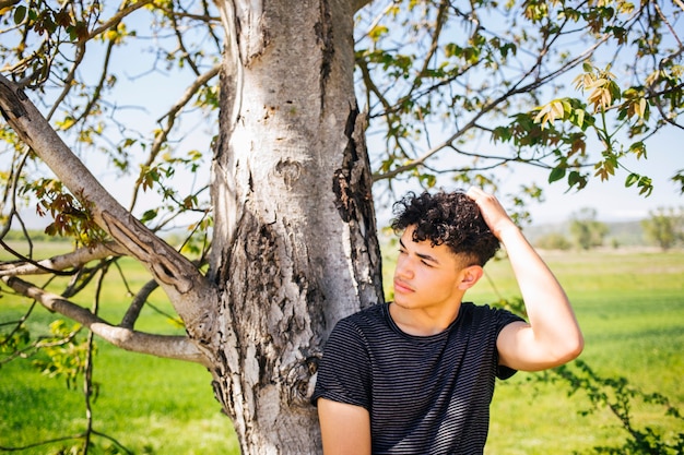 Retrato de hombre joven apoyado en el árbol y posando