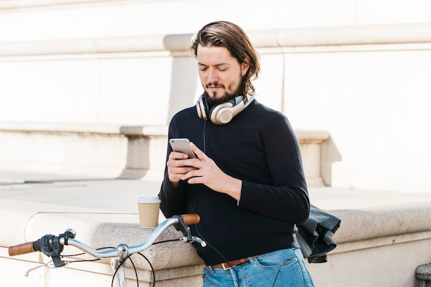 Foto gratuita retrato de un hombre joven con auriculares alrededor de su cuello usando un teléfono móvil al aire libre