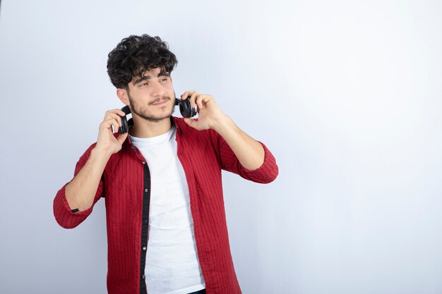 Retrato de hombre joven en auriculares escuchando canciones sobre pared blanca.