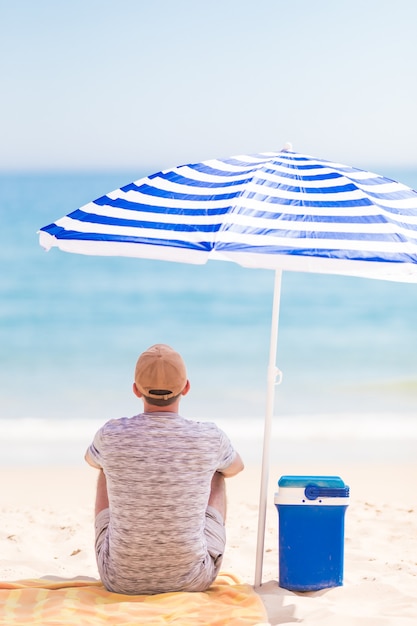Retrato de hombre joven con barba en una playa bajo una sombrilla en verano