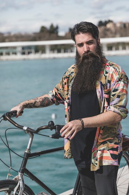 Retrato de hombre joven barbudo de pie con su bicicleta mirando a cámara