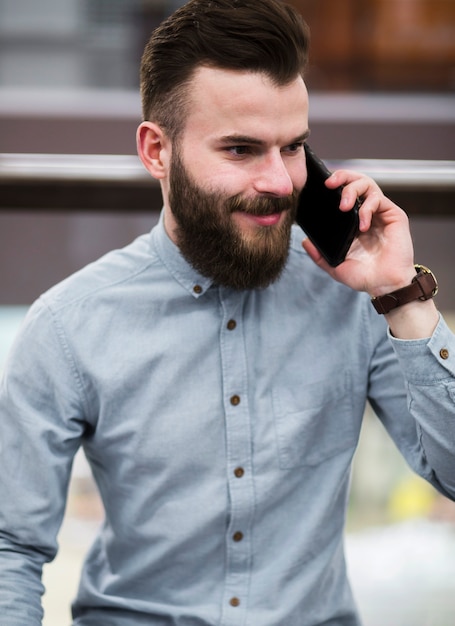 Foto gratuita retrato de un hombre joven barbudo sonriente que habla en el teléfono móvil