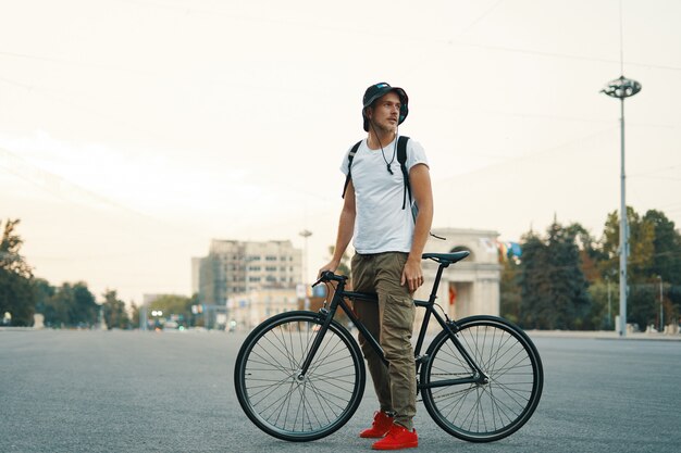 Retrato de hombre joven caminando con bicicleta cuidadosamente clásica en calles de la ciudad