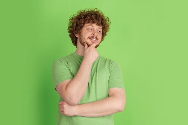 Retrato de hombre joven caucásico con brillantes emociones en estudio verde