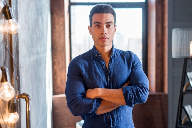 Retrato de un hombre joven confiado con sus brazos cruzados que miran la cámara