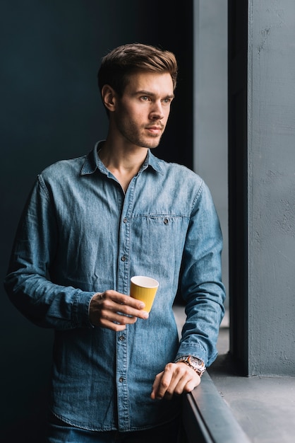 Retrato de un hombre joven contemplado que sostiene la taza de café disponible en la mano