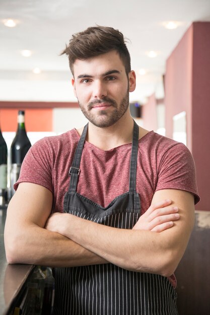 Retrato de hombre joven con delantal de pie en el bar