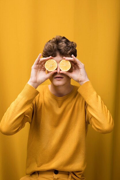 Retrato de hombre joven en un escenario amarillo con rodajas de limón enfrente de los ojos