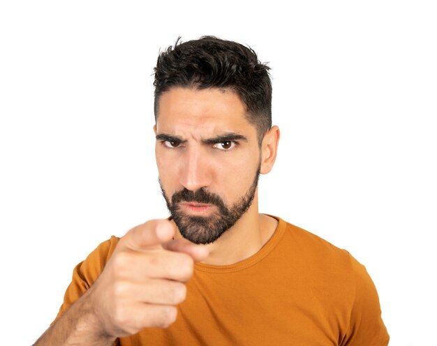 Retrato de hombre joven con expresión enojada y apuntando a alguien contra la pared blanca