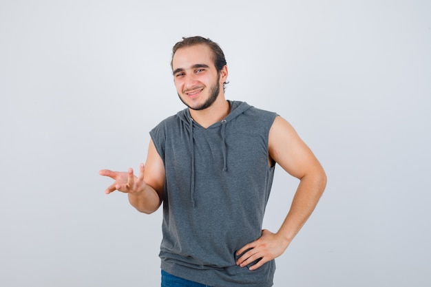 Retrato de hombre joven en forma estirando la mano hacia la cámara en una sudadera con capucha sin mangas y mirando la vista frontal alegre