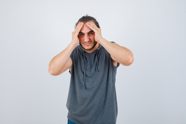 Retrato de hombre joven en forma que sufre de dolor de cabeza en sudadera con capucha sin mangas y mirando dolorosa vista frontal