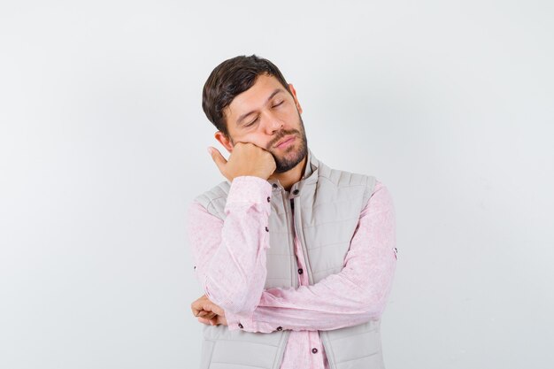 Retrato de hombre joven guapo apoyándose en la mejilla en el puño en camisa, chaleco y mirando soñoliento vista frontal