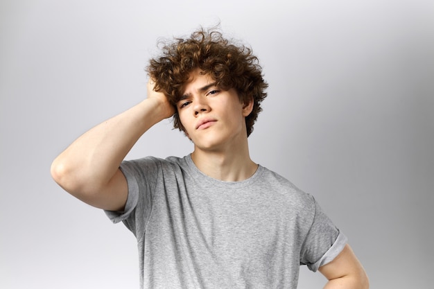 Retrato de hombre joven guapo de moda habiendo cansado o harto de expresión facial tocando su cabello castaño ondulado.