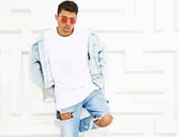 Foto gratuita retrato de hombre joven y guapo modelo vestido con jeans posando junto a la pared con textura blanca