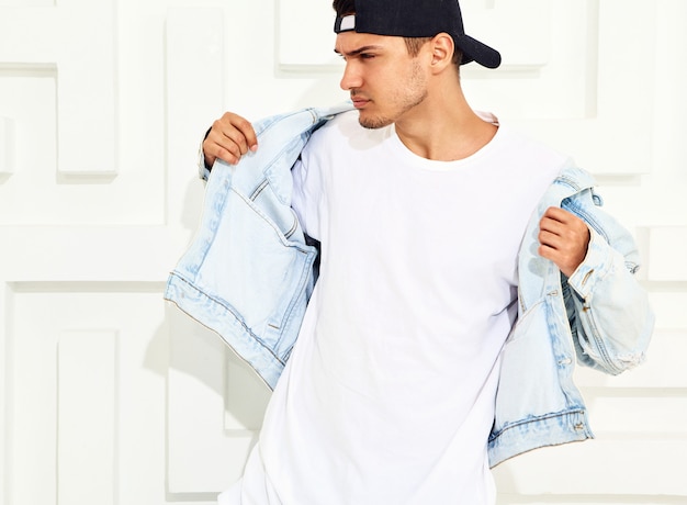 Retrato de hombre joven y guapo modelo vestido con jeans posando junto a la pared con textura blanca